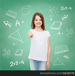 advertising, gesture, school, education and people - smiling little girl in white blank t-shirt pointing finger on you over green board background with doodles