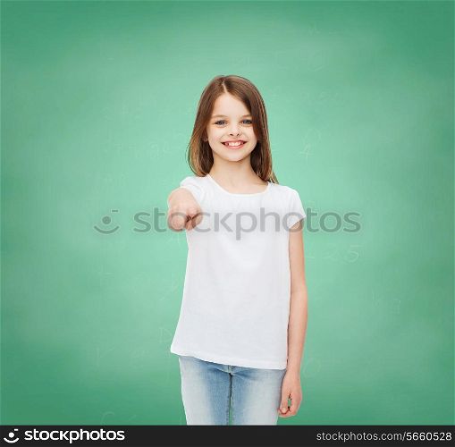 advertising, gesture, school, education and people - smiling little girl in white blank t-shirt over green board background