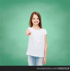 advertising, gesture, school, education and people - smiling little girl in white blank t-shirt over green board background