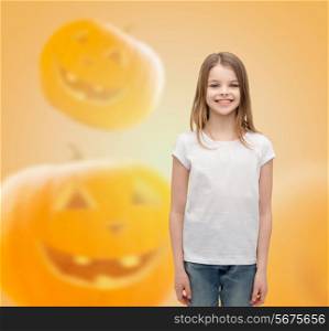 advertising, holidays and people concept - smiling little girl in white blank t-shirt over halloween pumpkins background