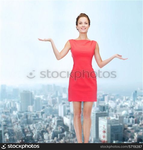 advertising, holidays and people concept - smiling young woman in red dress holding something on palm of her hands over city background
