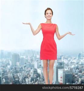 advertising, holidays and people concept - smiling young woman in red dress holding something on palm of her hands over city background