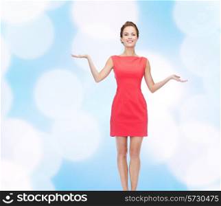 advertising, holidays and people concept - smiling young woman in red dress holding something on palm of her hands over blue lights background