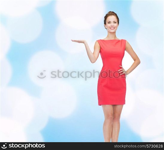 advertising, holidays and people concept - smiling young woman in red dress holding something on palm of her hand over blue lights background