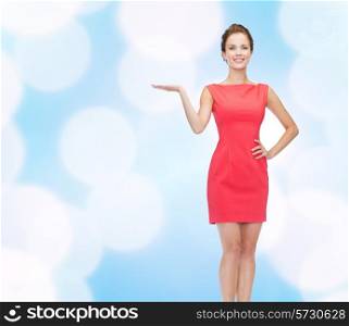 advertising, holidays and people concept - smiling young woman in red dress holding something on palm of her hand over blue lights background