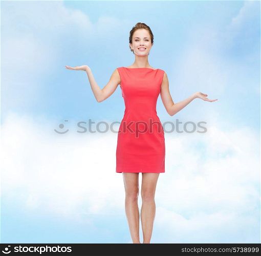 advertising, holidays and people concept - smiling young woman in red dress holding something on palm of her hands over blue cloudy sky background