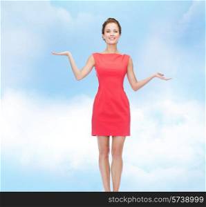 advertising, holidays and people concept - smiling young woman in red dress holding something on palm of her hands over blue cloudy sky background