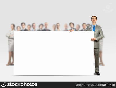 Advertising manager. Image of young man holding blank banner with crowd of business people at background