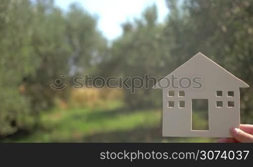 Advertising of houses for rent with copy space on the left. Close-up shot of woman hand with small house model and advert text on the background of green countryside on sunny day