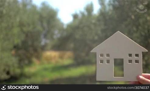 Advertising of houses for rent with copy space on the left. Close-up shot of woman hand with small house model and advert text on the background of green countryside on sunny day