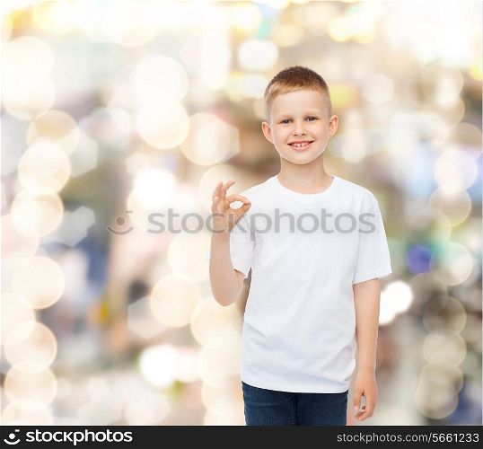 advertising, party, people and childhood concept - smiling little boy in white blank t-shirt making ok gesture over holidays background