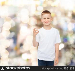 advertising, party, people and childhood concept - smiling little boy in white blank t-shirt making ok gesture over holidays background