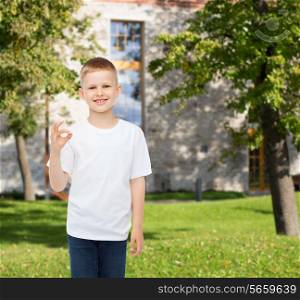 advertising, people and childhood concept - smiling little boy in white blank t-shirt making ok gesture over campus background