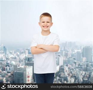 advertising, people and childhood concept - smiling little boy in white blank t-shirt over city background