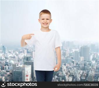 advertising, people and childhood concept - smiling little boy in white blank t-shirt pointing finger at himself over city background