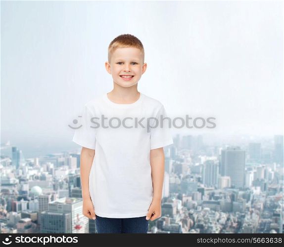 advertising, people and childhood concept - smiling little boy in white blank t-shirt over city background