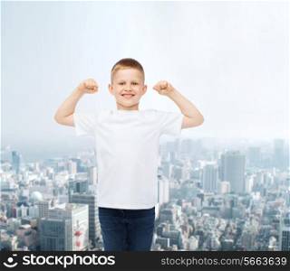 advertising, people and childhood concept - smiling little boy in white blank t-shirt with raised hands over city background