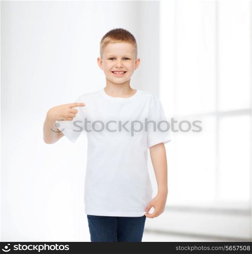 advertising, people, gesture and childhood concept - smiling boy in white blank t-shirt pointing fingers himself over white room background