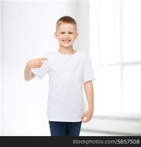 advertising, people, gesture and childhood concept - smiling boy in white blank t-shirt pointing fingers himself over white room background