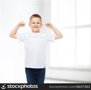 advertising, people, gesture and childhood concept - smiling little boy in white blank t-shirt with raised hands over white room background