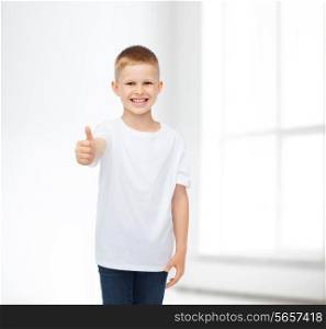 advertising, people, gesture and childhood concept - smiling little boy in white blank t-shirt showing thumbs up over white room background