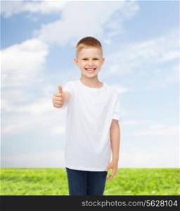 advertising, people, summer and childhood concept - smiling little boy in white blank t-shirt showing thumbs up over natural background