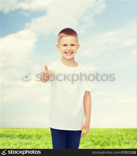 advertising, people, summer and childhood concept - smiling little boy in white blank t-shirt showing thumbs up over natural background