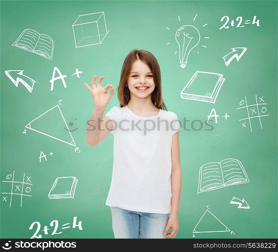 advertising, school, education, childhood and people - smiling little girl in white t-shirt showing ok sign over green board with doodles background