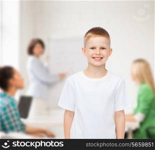 advertising, school, education, people and childhood concept - smiling little boy in white blank t-shirt over group of students in classroom