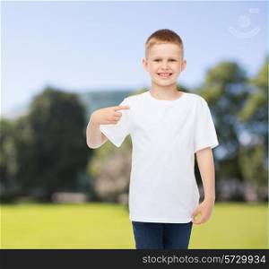 advertising, summer, people and childhood concept - smiling boy in white blank t-shirt pointing finger at himself over park background