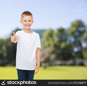 advertising, summer, people and childhood concept - smiling little boy in white blank t-shirt showing thumbs up over park background