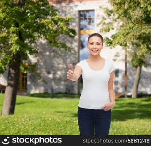 advertising, summer vacation, education, gesture and people concept - smiling young woman in blank white t-shirt showing thumbs up over campus background