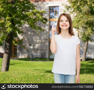 advertising, summer vacation, gesture, childhood and people - smiling little girl in white t-shirt pointing finger up over campus background