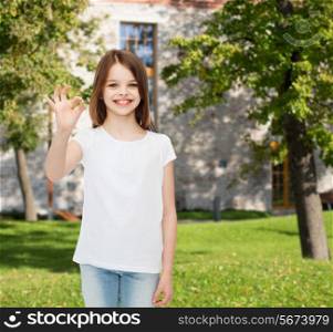 advertising, summer vacation, gesture, childhood and people - smiling little girl in white t-shirt showing ok sign over campus background