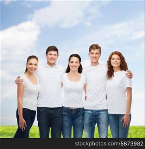 advertising, summer vacation, nature, friendship and people - group of smiling teenagers in white blank t-shirts over blue sky and grass background