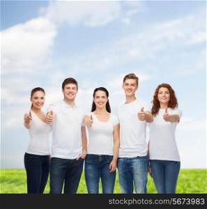 advertising, summer vacation, nature, friendship and people - group of smiling teenagers in white blank t-shirts showing thumbs up over blue sky and grass background