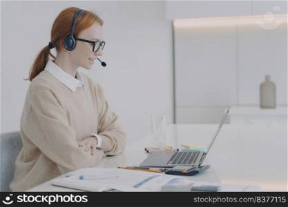 Adviser is working at laptop in office. Positive young woman is consultant of call center. European friendly girl in headset is talking to client. Customer support concept.. Adviser in headset is working at laptop in office. Young woman is consultant of call center.