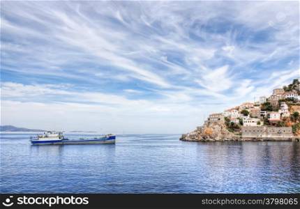 Aegean Sea and Greek island of Hydra or Ydra, a ship, and a dramatic blue and white cloudy sky in the Saronic Gulf, Aegean Sea, Greece.