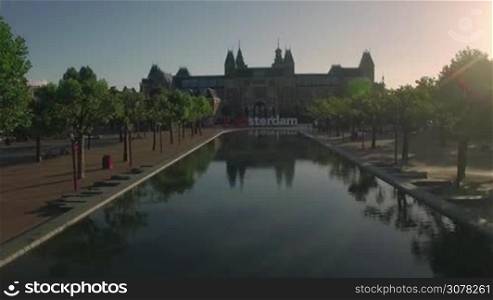 Aerial cityscape of Amsterdam at sunset with view to Rijksmuseum, Art Square with pond and I amsterdam slogan, Netherlands. Real time shot with speed-up rising in the middle