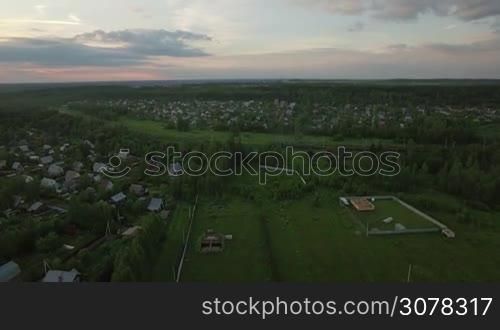 Aerial evening scene of dacha community in the countryside and cargo train running through it, Russia