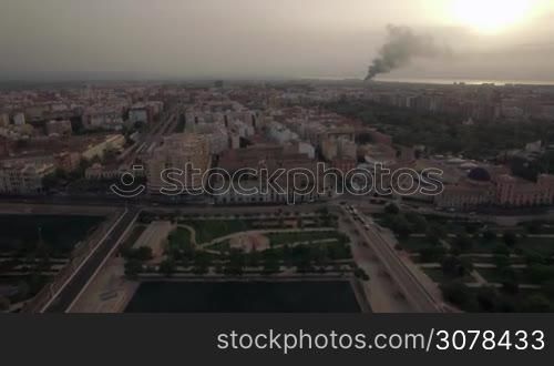 Aerial flight above sleeping Valencia district. View of the buildings, avenue, traffic, road, houses and parks against smoke on horizon, Valencia, Spain