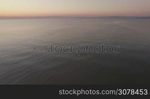 Aerial flight above the water of the sea against horizon line and clear sky at the sunset time