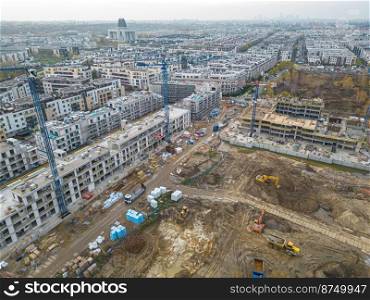 Aerial Flight Over a New Constructions Development Site with High Tower Cranes Building Real Estate. Heavy Machinery and Construction Workers are Employed. Top Down View at Contractors in Safety Hats.