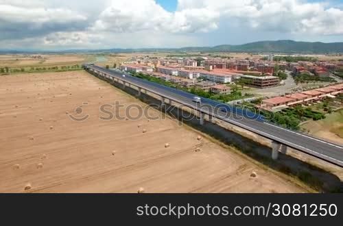 Aerial flight over the field with a view of the village and the bridge. Aerial view with scenic background of blue sky, clouds and the mountains. Tuscany, Italy