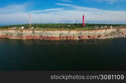 Aerial flying along the coast with a view of the coastline with cliffs from the sea and on land The Old Lighthouse and the wind turbines