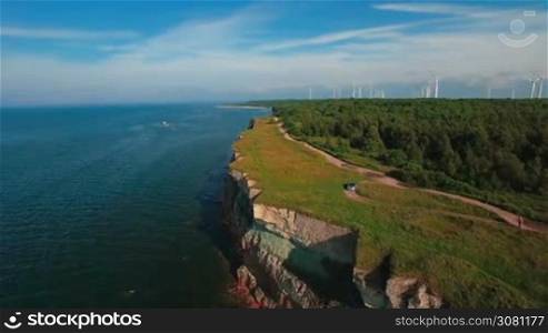 Aerial flying along the coast with a view of the coastline with cliffs from the sea and on land The Old Lighthouse and the power of wind turbines, green energy