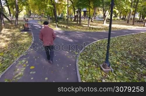 Aerial footage of elderly man walking alone in the park in autumn.