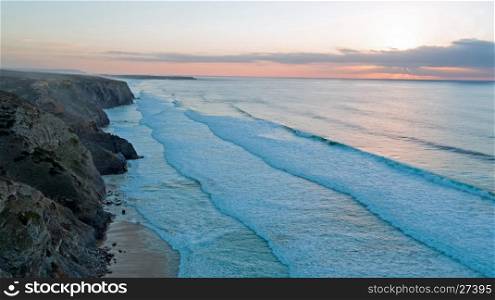 Aerial from rocks and ocean at Praia Vale Figueiras in Portugal at twilight