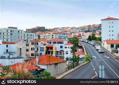 Aerial Funchal cityscape, traffic on hill road, residential houses with red rooftops, Madeira, Portugal
