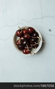 Aerial image of a bowl filled with cherries over a white marble table, fresh food, wellness, healthy food